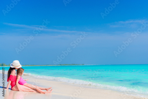 Little girl and young mother at tropical beach sitting in shallow water