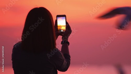 Woman taking photograph of twilight sunset and seagulls on the Bang Pu beach , Samut Prakan , Thailand