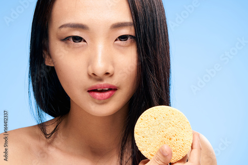 Beautiful young woman on a blue background holds a sponge for make-up removal, asian