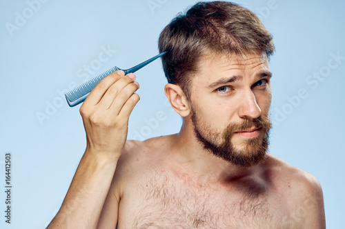 Young guy with a beard on a blue background holds a comb