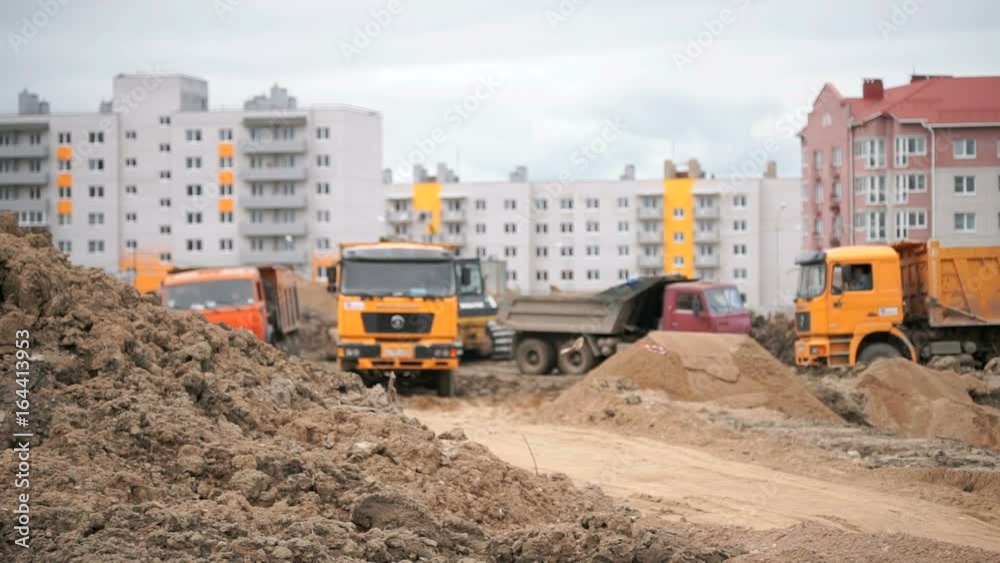 Construction site. Dump trucks working on a construction site carry clay from one object to another in summer Construction site. Dump trucks working on a construction site carry clay from one object to another in summer