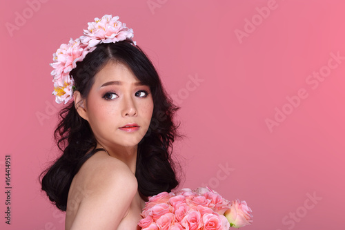 Beautiful Asian Woman black hair with flora crowd, holding bouquet artificial rose over chest photo