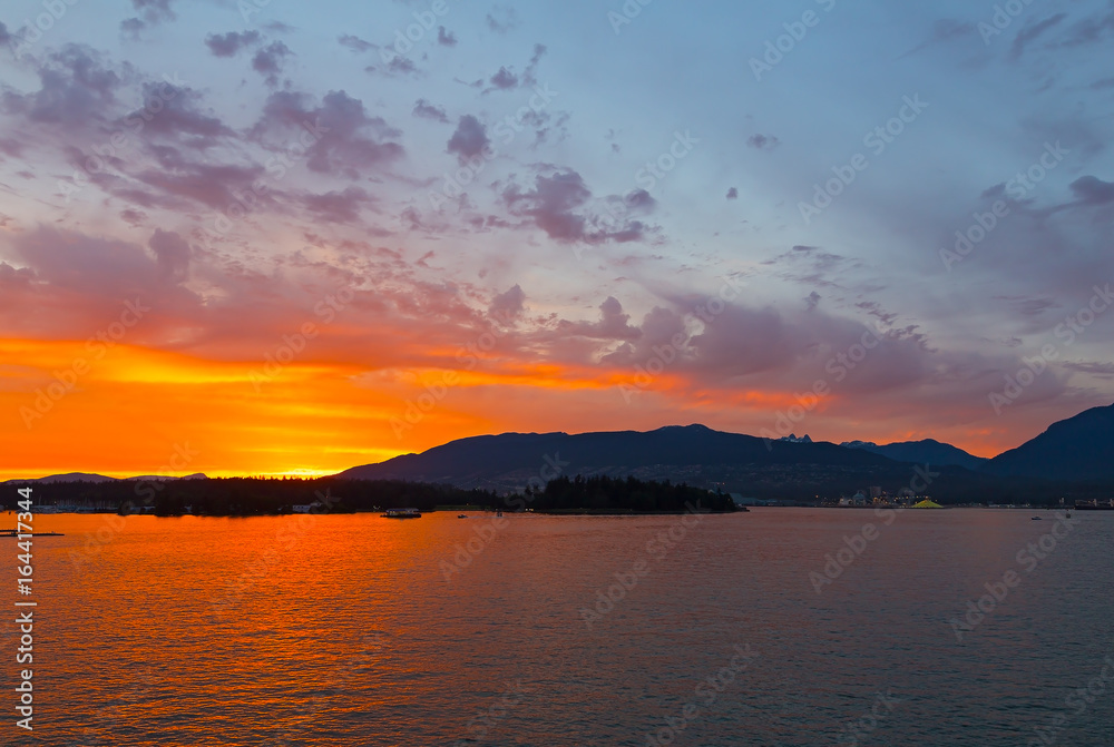 Spectacular sunset in city of Vancouver, BC, Canada. Mountains on horizon during sunset over the sea.