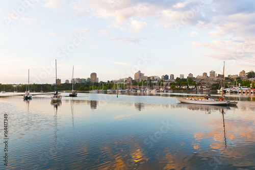 Yachts on the water in early morning and urban landscape on horizon. Sunrise touched water surface of False Creek in Vancouver, Canada.