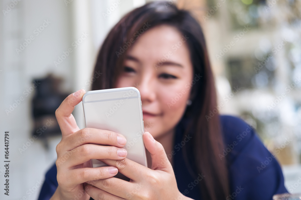 Beautiful Asian woman with smiley face using and looking at smart phone in modern cafe Beautiful Asian woman with smiley face using and looking at smart phone in modern cafe