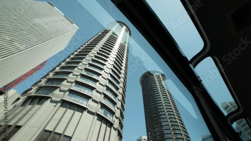 Tall city buildings pass by a mono rail window view.  