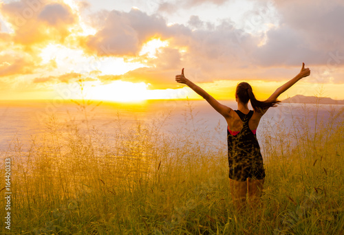 People wining concept. Fit female looking at the sunset with her arms up in the air celebrating 
