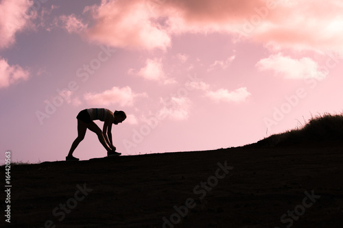 Silhouette of female runner tying her shoe.  © kieferpix