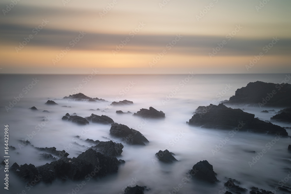 Beautiful long exposure landscape image of sea over rocks during vibrant sunset