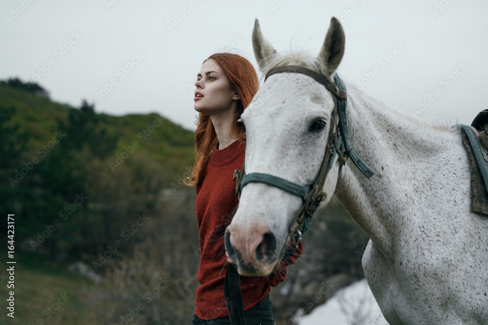 Obraz premium Beautiful young woman walking in the mountains with a horse