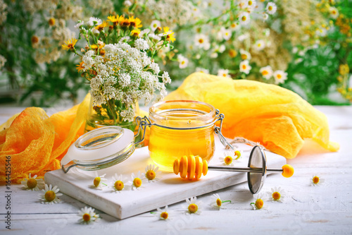 Tasty and healthy honey on white wooden table with flowers of chamomile.