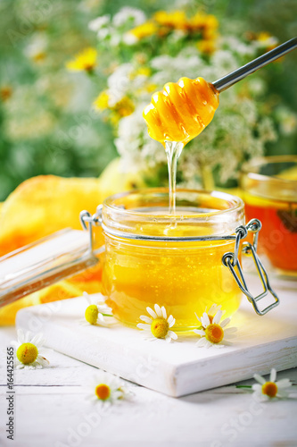 Tasty and healthy honey on white wooden table with flowers of chamomile.