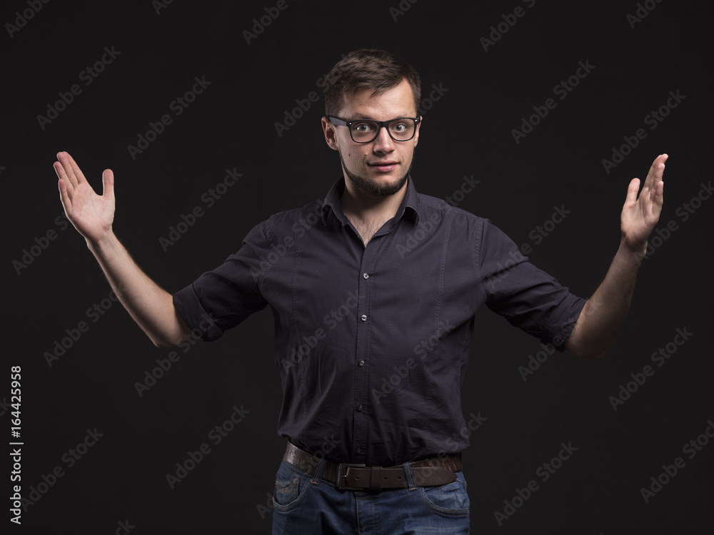 Young pensive man portrait of a confident businessman showing by hands on a black background. Ideal for banners, registration forms, presentation, landings, presenting concept. Young pensive man portrait of a confident businessman showing by hands on a black background. Ideal for banners, registration forms, presentation, landings, presenting concept.
