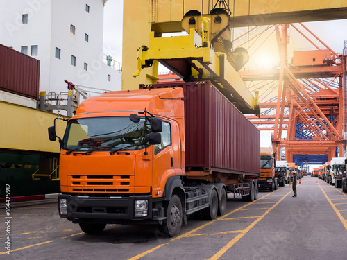 The truck is queuing to pick up container from the vessel by port crane.