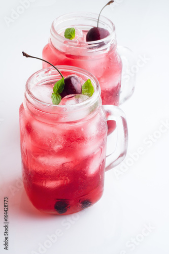 Two glass mugs with red drink, berries and ice close-up on a white background.