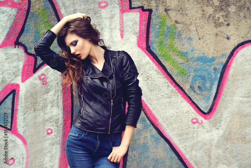 Portrait of the beautiful young woman with wavy brown hair posing outdoor, over graffiti background. Toned.