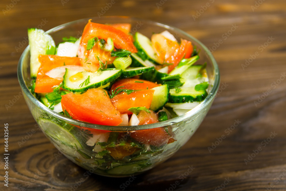 Fresh salad with tomato, cucumber, onion, parsley and dill in glass bowl on wooden table Fresh salad with tomato, cucumber, onion, parsley and dill in glass bowl on wooden table