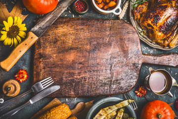 Thanksgiving dinner background with  turkey ,sauce,grilled vegetables,corn ,cutlery ,  pumpkin, fall leaves and flowers arrangements around wooden gutting board, top view.