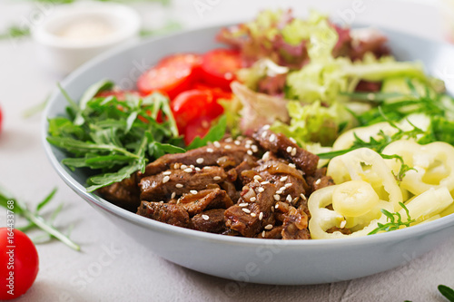 Salad with beef teriyaki and fresh vegetables - tomatoes  cucumbers  paprika  arugula and lettuce in bowl.