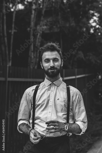 Young man with a beard and cigar dressed fashionable in modern clothes with suspenders.