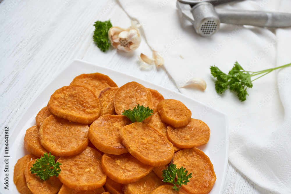 Baked sweet potatoes in white plate on a white wooden table with parsley, garlic and salt. White wooden rustic picnic table scenery from above. Baked sweet potatoes in white plate on a white wooden table with parsley, garlic and salt. White wooden rustic picnic table scenery from above.