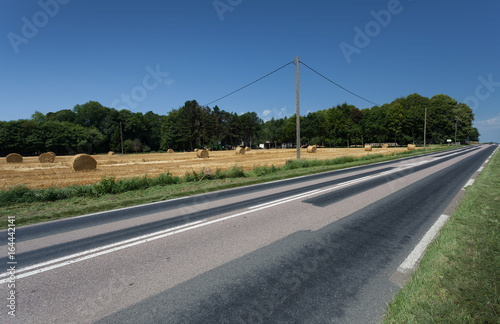 Φωτογραφία A repaired and pot hole free country road alongside a field of hay bales in Norm