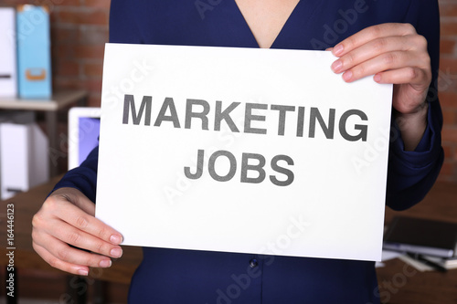 Woman holding paper sheet with text MARKETING JOBS