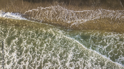 Vista aerea perpendicolare delle onde del mar Tirreno che si infrangono sulla costa. L' impatto con il bagnasciuga crea la schiuma bianca. La spiaggia d'inverno è vuota.