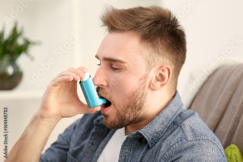 Young man using inhaler for asthma and respiratory diseases at home