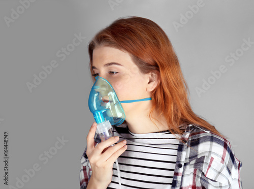 Young woman using nebulizer for asthma and respiratory diseases on light background