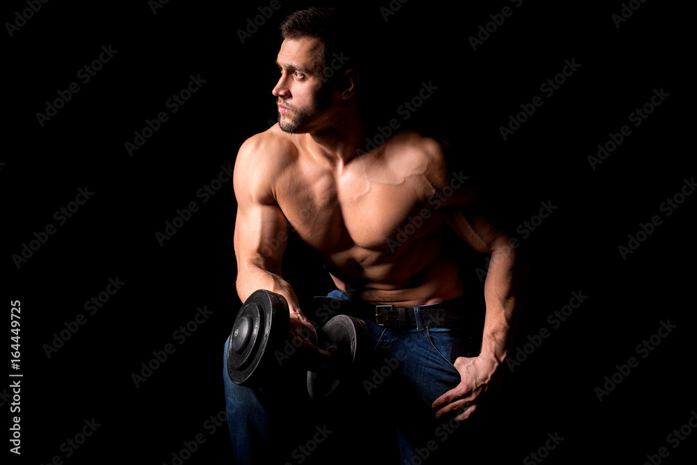 Strong man with muscular body working out. Weight exercise with dumbbell on black background.