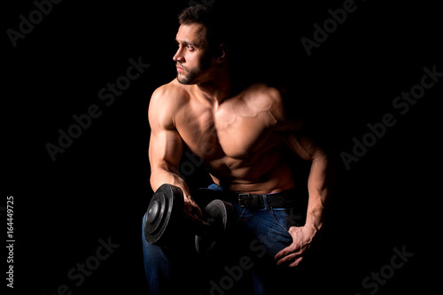 Strong man with muscular body working out. Weight exercise with dumbbell on black background.