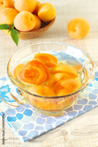 Canned apricots in glass bowl and fresh apricots with leaves