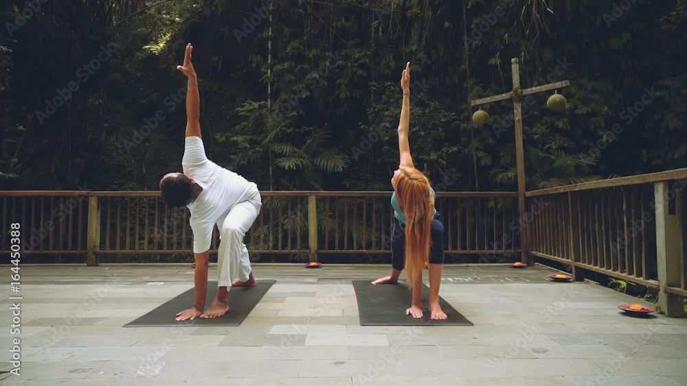 Balinese yoga teacher and caucasian woman doing warrior pose and extended side angle pose Balinese yoga teacher and caucasian woman doing warrior pose and extended side angle pose