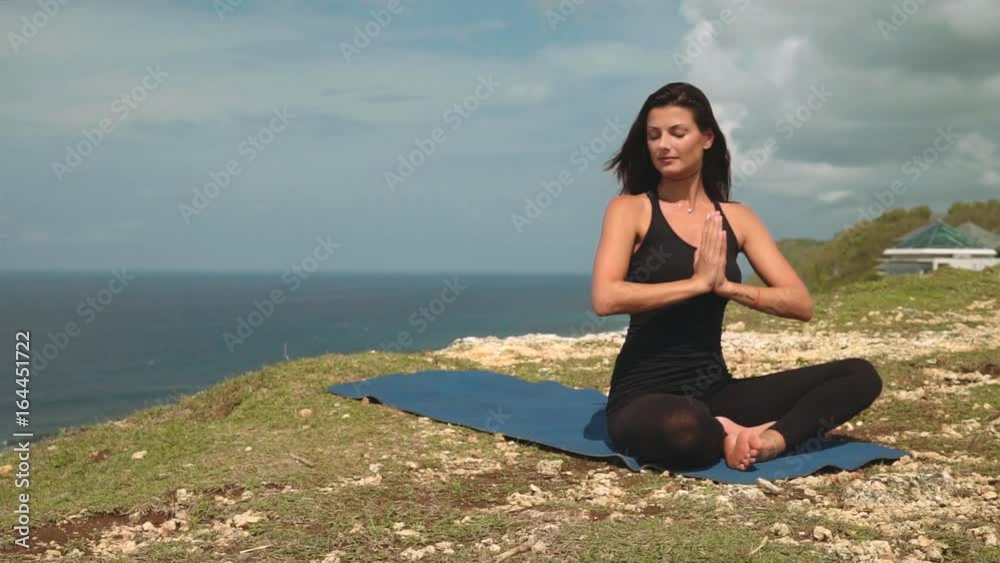 Beautiful woman in black meditating on edge of cliff on Bali shore