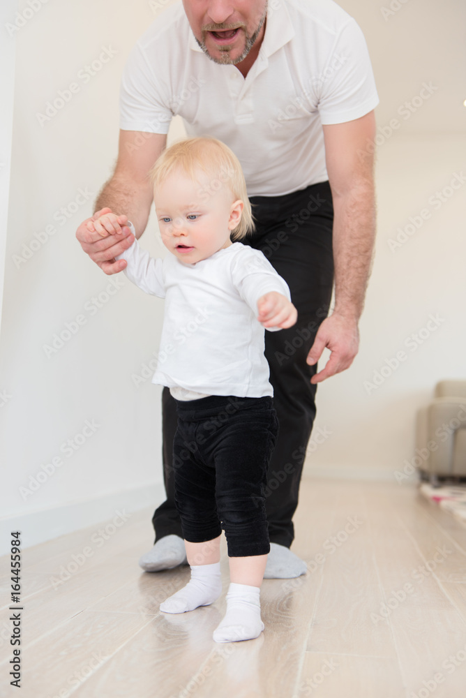 Happy family enjoying at home. Father and his beautiful baby girl playing and learning how to walk. Family values. Leisure together. Happy family enjoying at home. Father and his beautiful baby girl playing and learning how to walk. Family values. Leisure together.