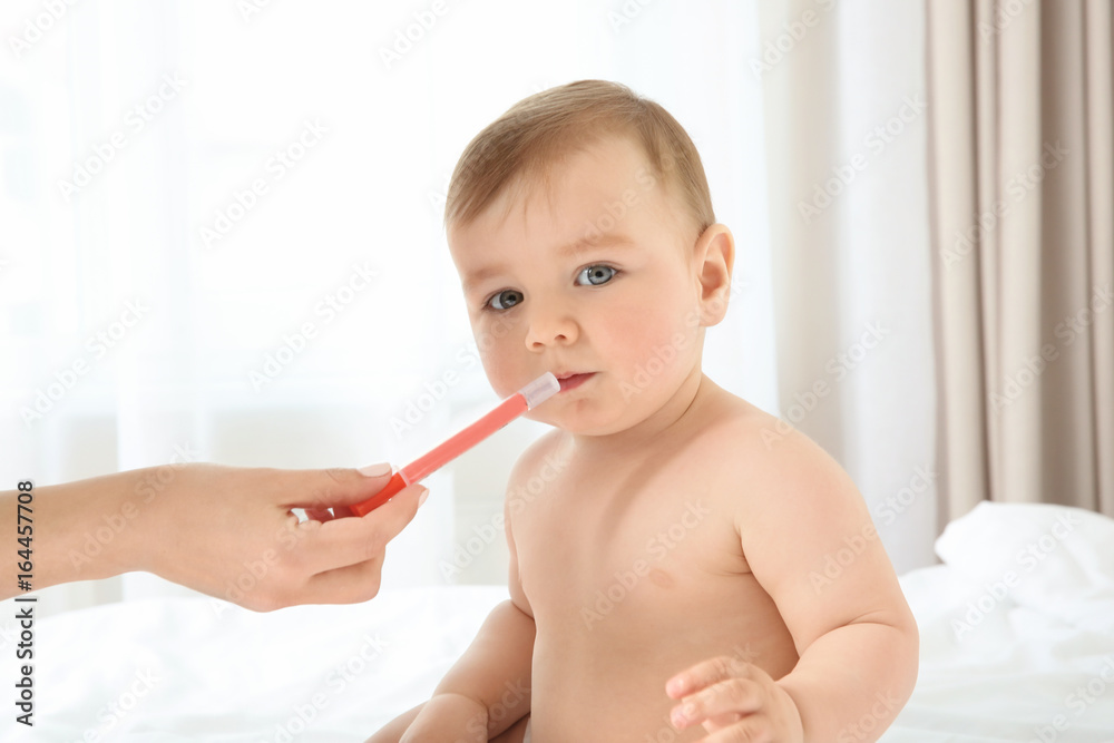 Mother holding oral dosing syringe and cute little baby sitting on bed at home. Health care concept Mother holding oral dosing syringe and cute little baby sitting on bed at home. Health care concept
