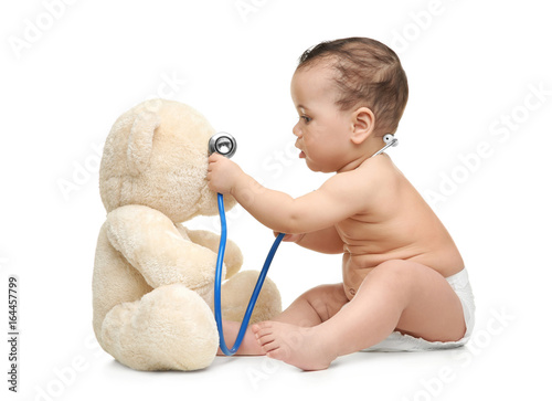 Cute little baby playing with stethoscope and toy bear on white background. Health care concept photo