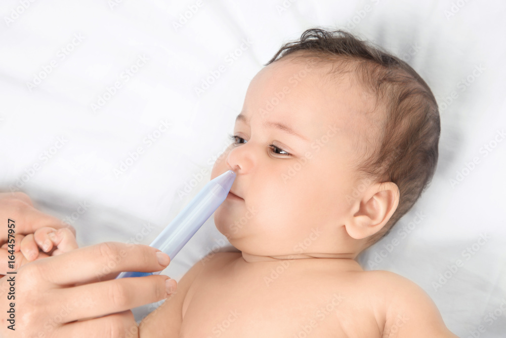 Mother using nasal aspirator for cute little baby lying on bed at home. Health care concept Mother using nasal aspirator for cute little baby lying on bed at home. Health care concept