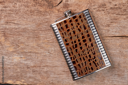 Stylish brown hip flask, wooden background. Steel jhip flask as souvenir.