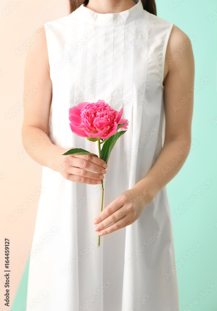 Young woman holding beautiful peony flower on color background