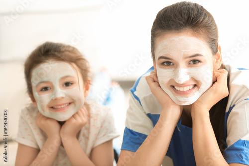Young woman and her little daughter with facial masks at home