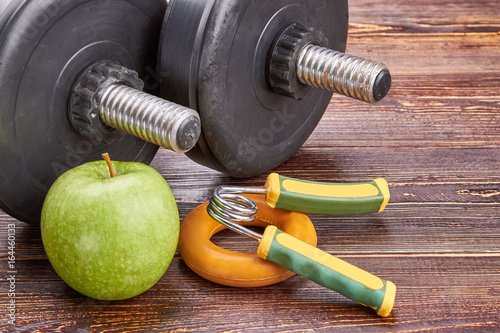 Healthy lifystyle concept. Dumbbells, green apple, expanders, wooden background.