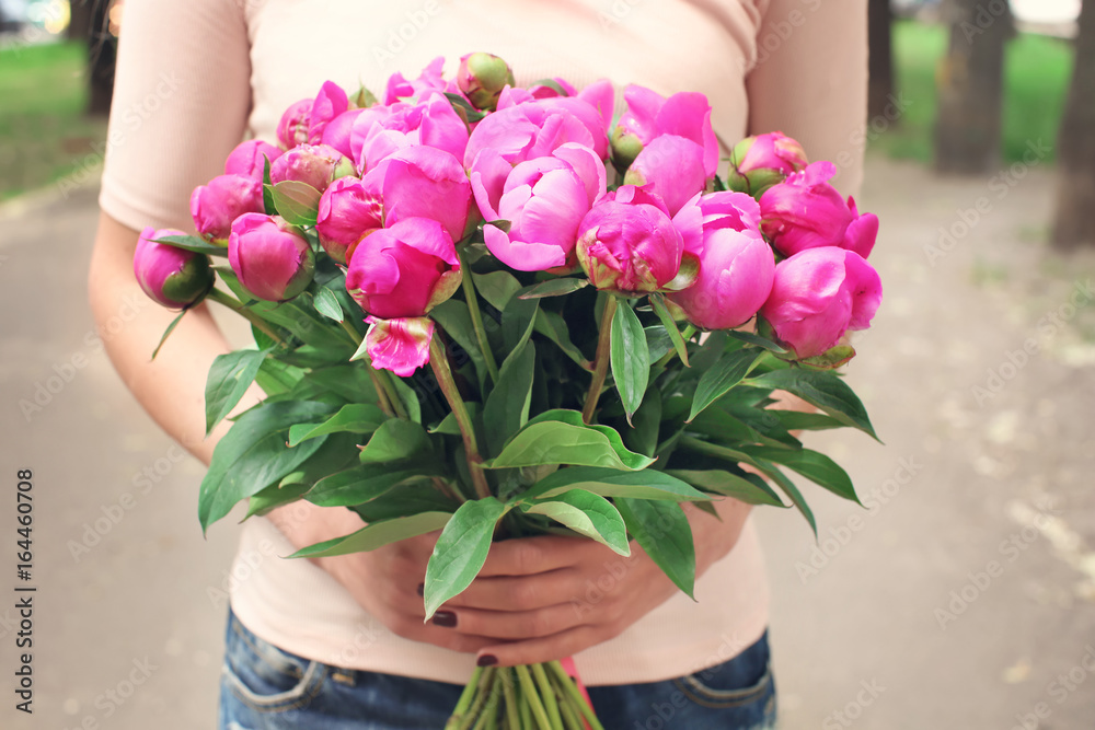 Young woman holding bouquet with beautiful peonies on street