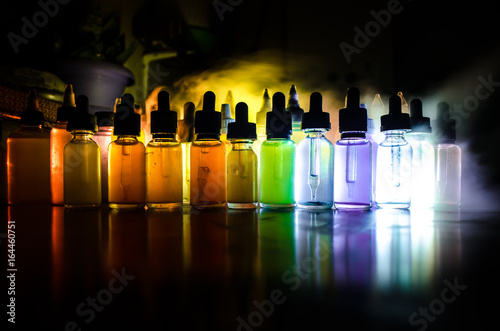 Vape concept. Smoke clouds and vape liquid bottles on dark background. Light effects. Useful as background or vape advertisement or vape background. Selective focus