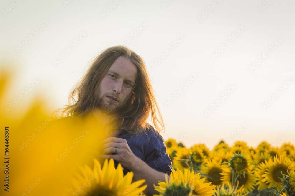 Young caucasian - nordic man with blond and long hairs among sunflowers field Young caucasian - nordic man with blond and long hairs among sunflowers field
