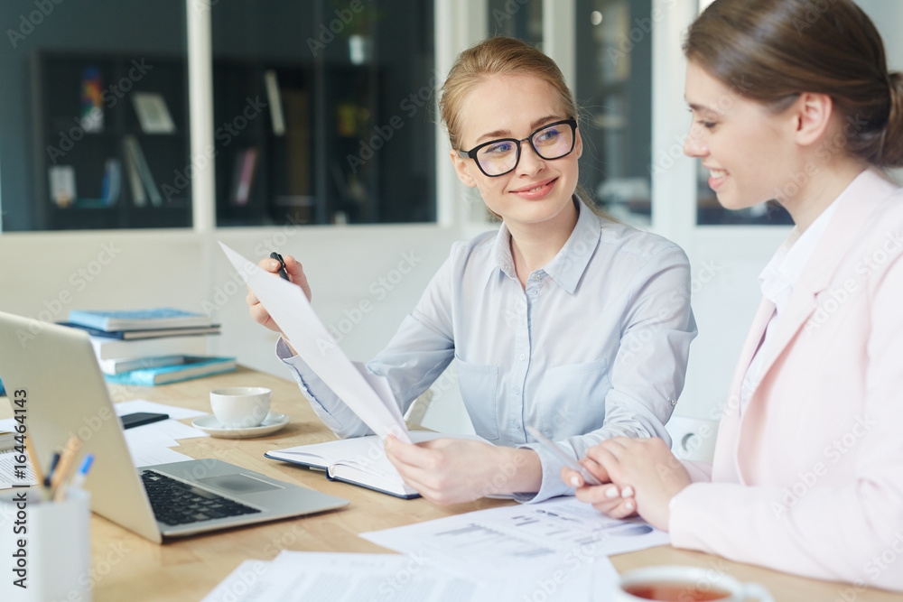 Obraz premium Young businesswoman pointing at document while talking to co-worker