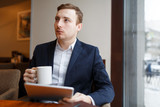 Pensive businessman with mug and touchpad networking in cafe