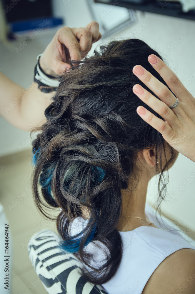 Naklejka premium Closeup of a professional hairdresser's hands doing a hairstyle in a beauty salon. Model of a brunette with long hair. The concept of fashionable stylish hairstyle, professional work with hair.