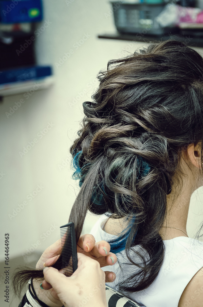 Naklejka premium Closeup of a professional hairdresser's hands doing a hairstyle in a beauty salon. Model of a brunette with long hair. The concept of fashionable stylish hairstyle, professional work with hair.